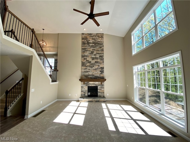 unfurnished living room with high vaulted ceiling, ceiling fan with notable chandelier, carpet, and a fireplace