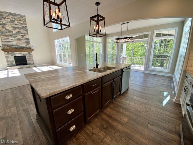 kitchen featuring open floor plan, stainless steel dishwasher, a fireplace, pendant lighting, and a sink