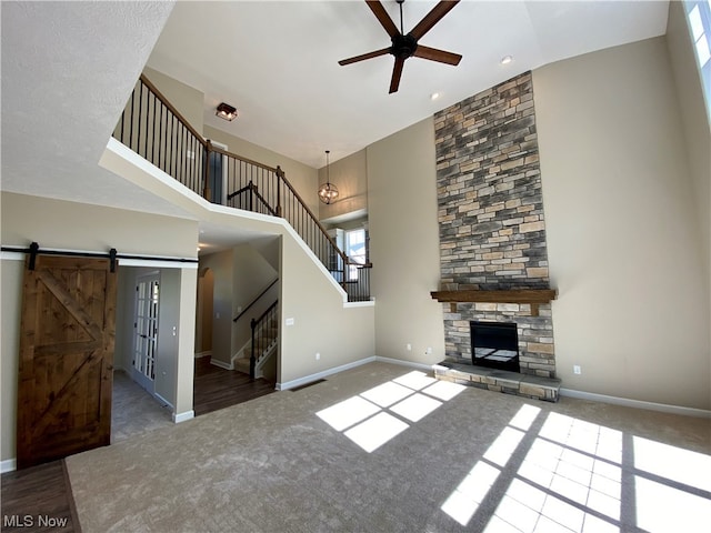 unfurnished living room with a stone fireplace, a towering ceiling, carpet flooring, ceiling fan, and a barn door