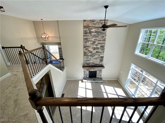 living room with a stone fireplace, plenty of natural light, light colored carpet, and high vaulted ceiling