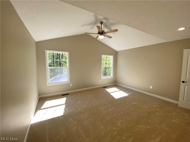 carpeted empty room featuring vaulted ceiling, ceiling fan, visible vents, and baseboards