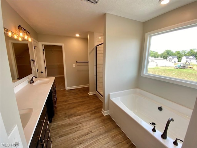 bathroom with a garden tub, double vanity, a sink, a shower stall, and wood finished floors