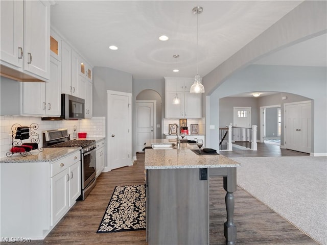 kitchen with stainless steel appliances, arched walkways, white cabinets, and decorative light fixtures