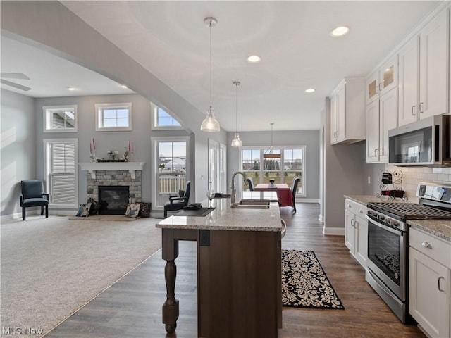 kitchen featuring appliances with stainless steel finishes, open floor plan, decorative light fixtures, light stone countertops, and a sink