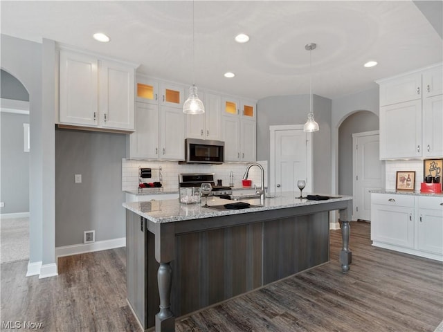 kitchen featuring arched walkways, stove, white cabinetry, stainless steel microwave, and glass insert cabinets