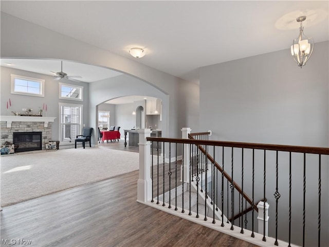 hallway featuring arched walkways, a notable chandelier, an upstairs landing, wood finished floors, and baseboards