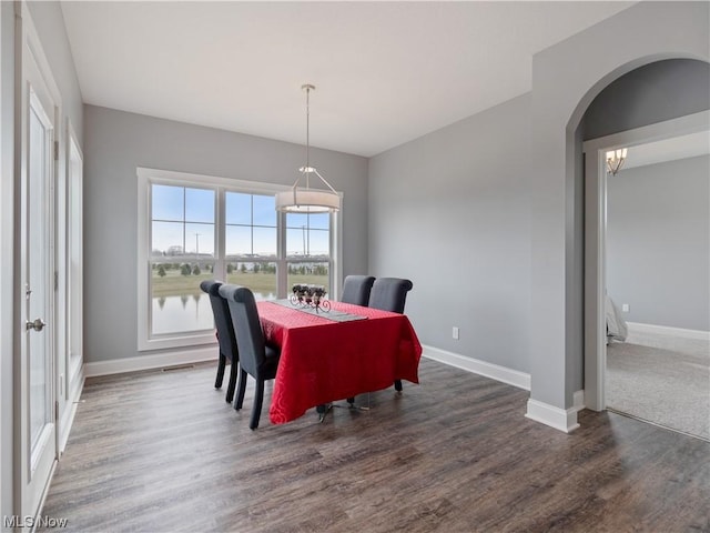 dining space with dark wood-style floors, baseboards, and arched walkways