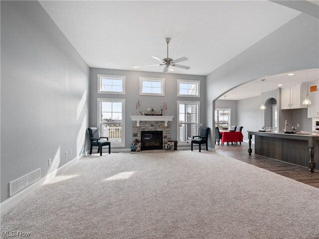 unfurnished living room with arched walkways, a fireplace, visible vents, dark carpet, and a towering ceiling