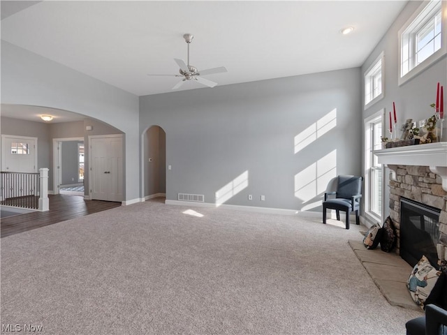 living room with dark carpet, visible vents, arched walkways, and a stone fireplace