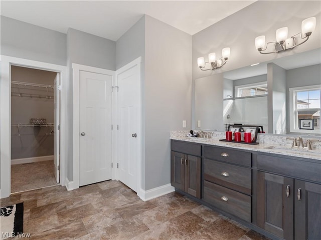 full bath with double vanity, a sink, a walk in closet, and baseboards