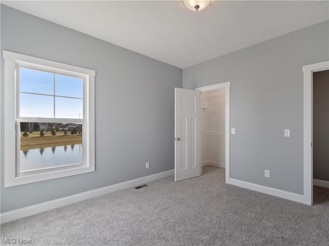 unfurnished bedroom featuring a spacious closet, carpet, visible vents, and baseboards