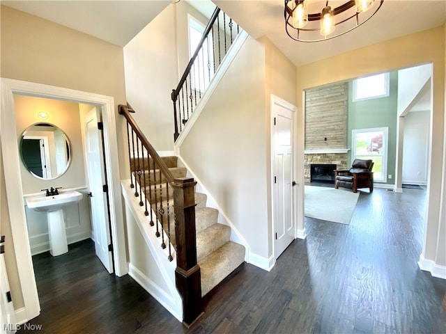 staircase featuring hardwood / wood-style floors, an inviting chandelier, sink, a towering ceiling, and a tiled fireplace