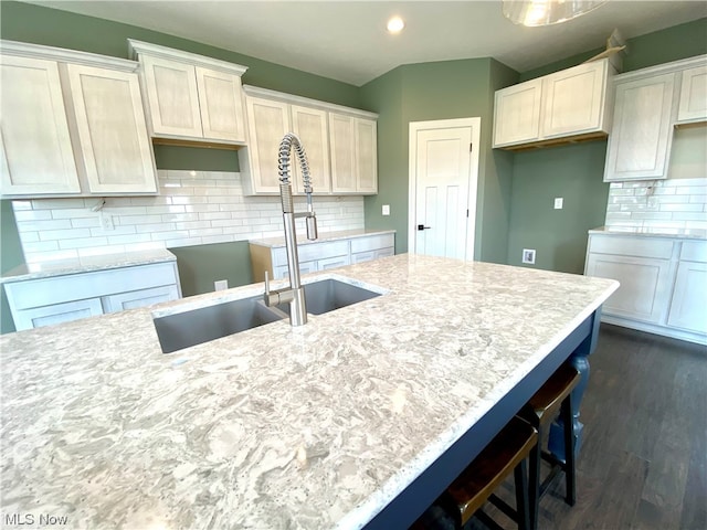 kitchen with dark hardwood / wood-style floors, light stone countertops, sink, and backsplash