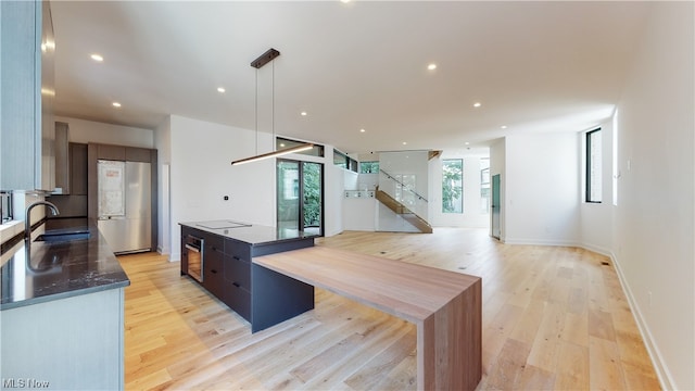 kitchen with hanging light fixtures, a kitchen island, black electric stovetop, sink, and light hardwood / wood-style flooring