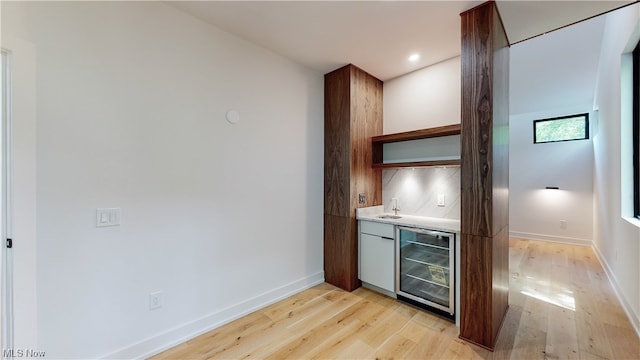 bar with wine cooler, light hardwood / wood-style flooring, tasteful backsplash, and sink