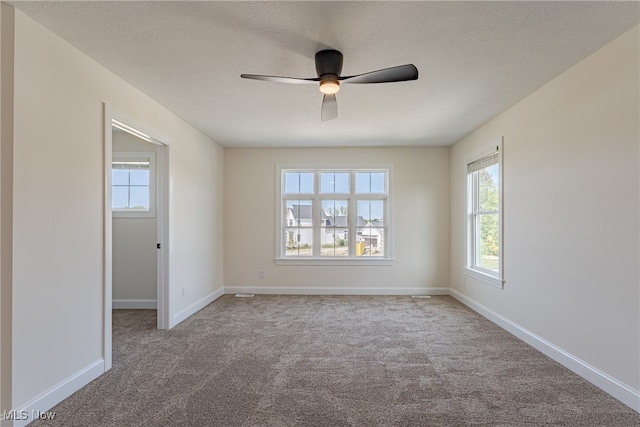 unfurnished room with light colored carpet, a wealth of natural light, ceiling fan, and a textured ceiling