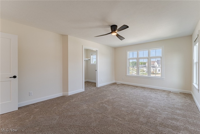 unfurnished bedroom featuring light colored carpet, ceiling fan, a walk in closet, and a closet