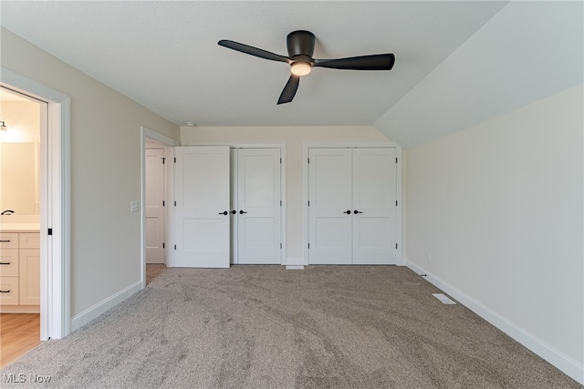 unfurnished bedroom featuring two closets, light colored carpet, lofted ceiling, ceiling fan, and connected bathroom