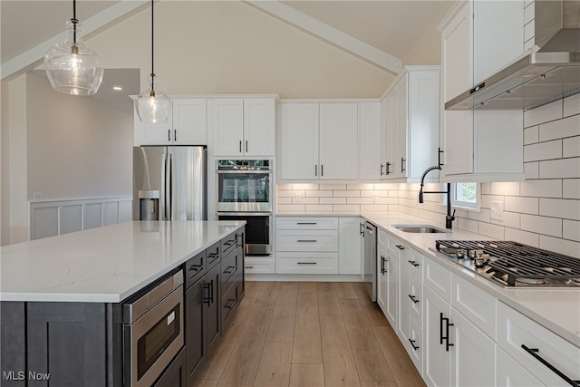 kitchen featuring white cabinets, appliances with stainless steel finishes, wall chimney exhaust hood, a kitchen island, and vaulted ceiling with beams