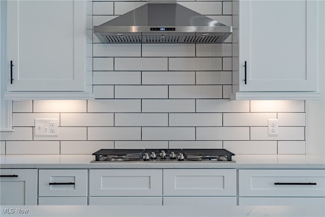 kitchen featuring wall chimney range hood, stainless steel gas stovetop, decorative backsplash, and white cabinetry