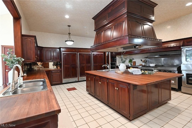 kitchen featuring pendant lighting, sink, a textured ceiling, butcher block countertops, and custom range hood