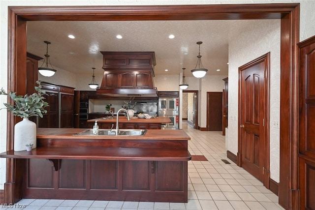 kitchen featuring sink, hanging light fixtures, light tile patterned floors, double oven, and a kitchen bar