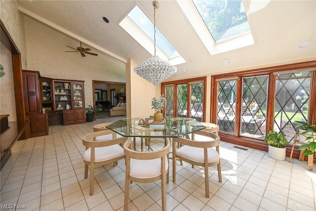 dining room with a skylight, light tile patterned floors, ceiling fan with notable chandelier, and high vaulted ceiling