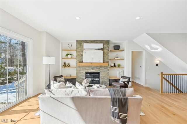 living room featuring built in shelves, a fireplace, and light hardwood / wood-style flooring