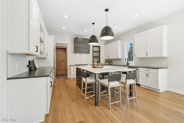 kitchen featuring white cabinets, a center island, wall chimney range hood, light wood-type flooring, and a breakfast bar