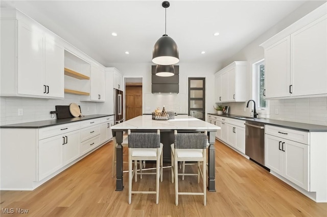 kitchen with light hardwood / wood-style floors, appliances with stainless steel finishes, decorative light fixtures, a kitchen island, and white cabinets