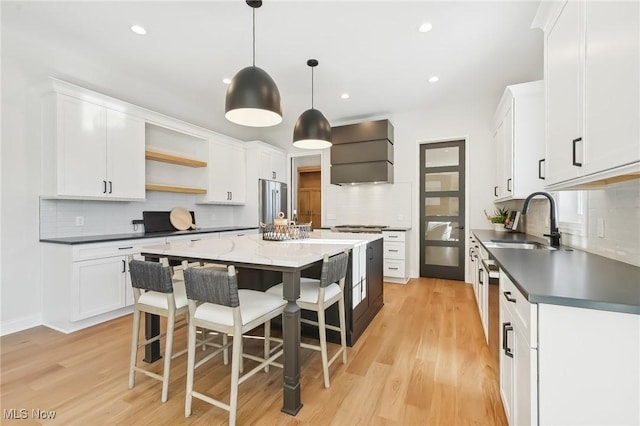 kitchen featuring white cabinets, a center island, sink, hanging light fixtures, and light hardwood / wood-style flooring