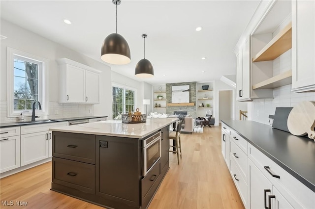 kitchen with decorative light fixtures, stainless steel microwave, sink, white cabinetry, and light wood-type flooring