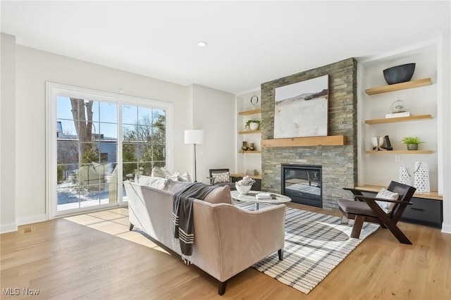 living room with built in features, a stone fireplace, and light hardwood / wood-style flooring