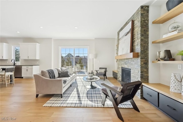 living room with sink, a stone fireplace, and light wood-type flooring