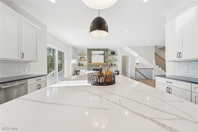 kitchen featuring a fireplace, dark stone countertops, stainless steel dishwasher, and decorative light fixtures