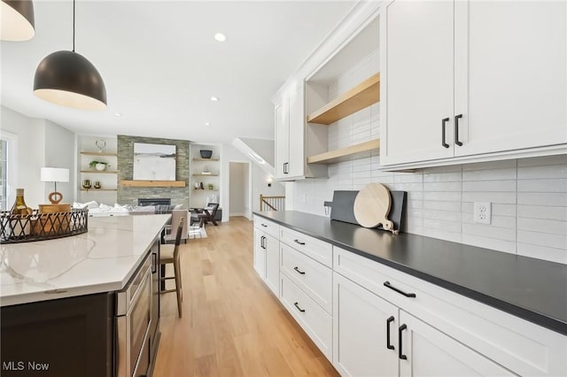 kitchen with white cabinets, decorative light fixtures, dark stone counters, decorative backsplash, and light wood-type flooring