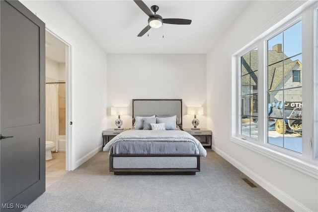 bedroom featuring ceiling fan, ensuite bathroom, and light colored carpet