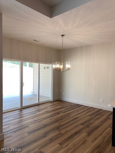 unfurnished room featuring an inviting chandelier, dark wood-type flooring, and a textured ceiling