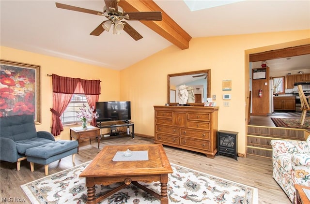 living room featuring vaulted ceiling with beams, light hardwood / wood-style floors, a wood stove, and ceiling fan