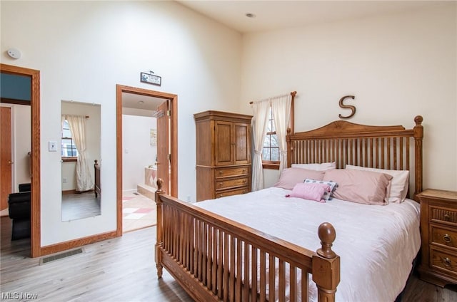 bedroom featuring ensuite bathroom, light wood-type flooring, and a towering ceiling