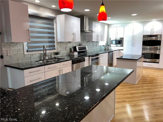 kitchen featuring appliances with stainless steel finishes, wall chimney exhaust hood, light hardwood / wood-style floors, tasteful backsplash, and decorative light fixtures