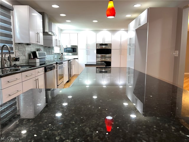 kitchen with appliances with stainless steel finishes, sink, light hardwood / wood-style floors, tasteful backsplash, and dark stone countertops