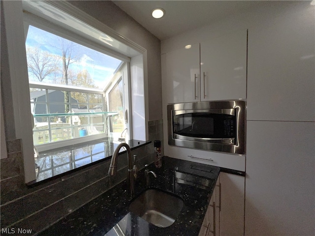 kitchen with dark stone countertops, sink, and stainless steel microwave