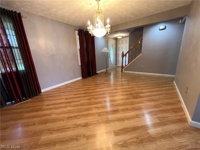 spare room featuring a textured ceiling, a notable chandelier, and hardwood / wood-style floors