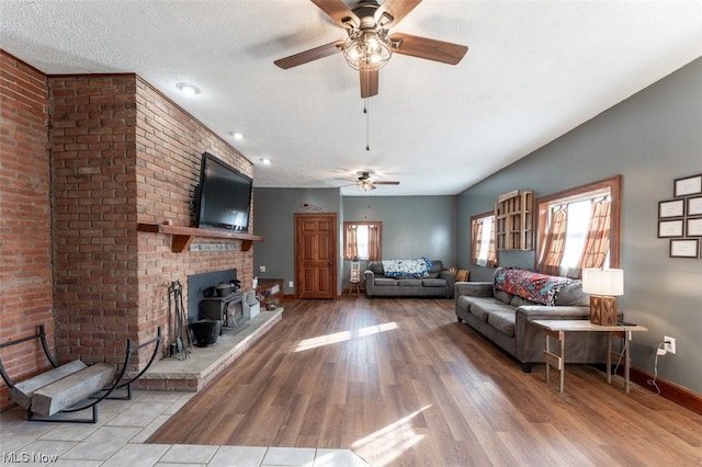 living room featuring a textured ceiling, ceiling fan, light hardwood / wood-style floors, and a wood stove