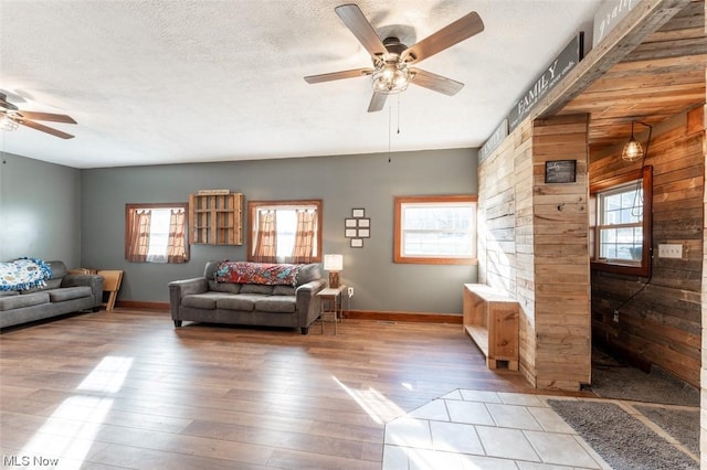 living room featuring ceiling fan, a healthy amount of sunlight, light wood-type flooring, and wooden walls