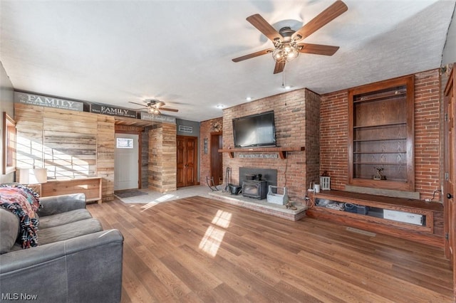 living room featuring a textured ceiling, wood-type flooring, built in shelves, a wood stove, and ceiling fan