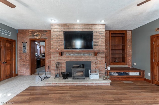 living room with ceiling fan, a wood stove, a textured ceiling, and hardwood / wood-style flooring