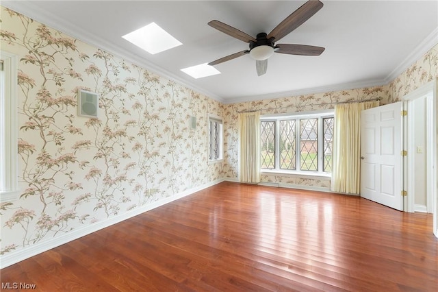 empty room with a skylight, hardwood / wood-style flooring, crown molding, and ceiling fan