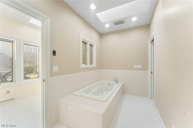 bathroom featuring tile patterned flooring, a skylight, and tiled tub